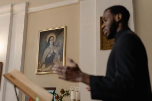 A priest delivers a sermon inside a church with religious art in the background.