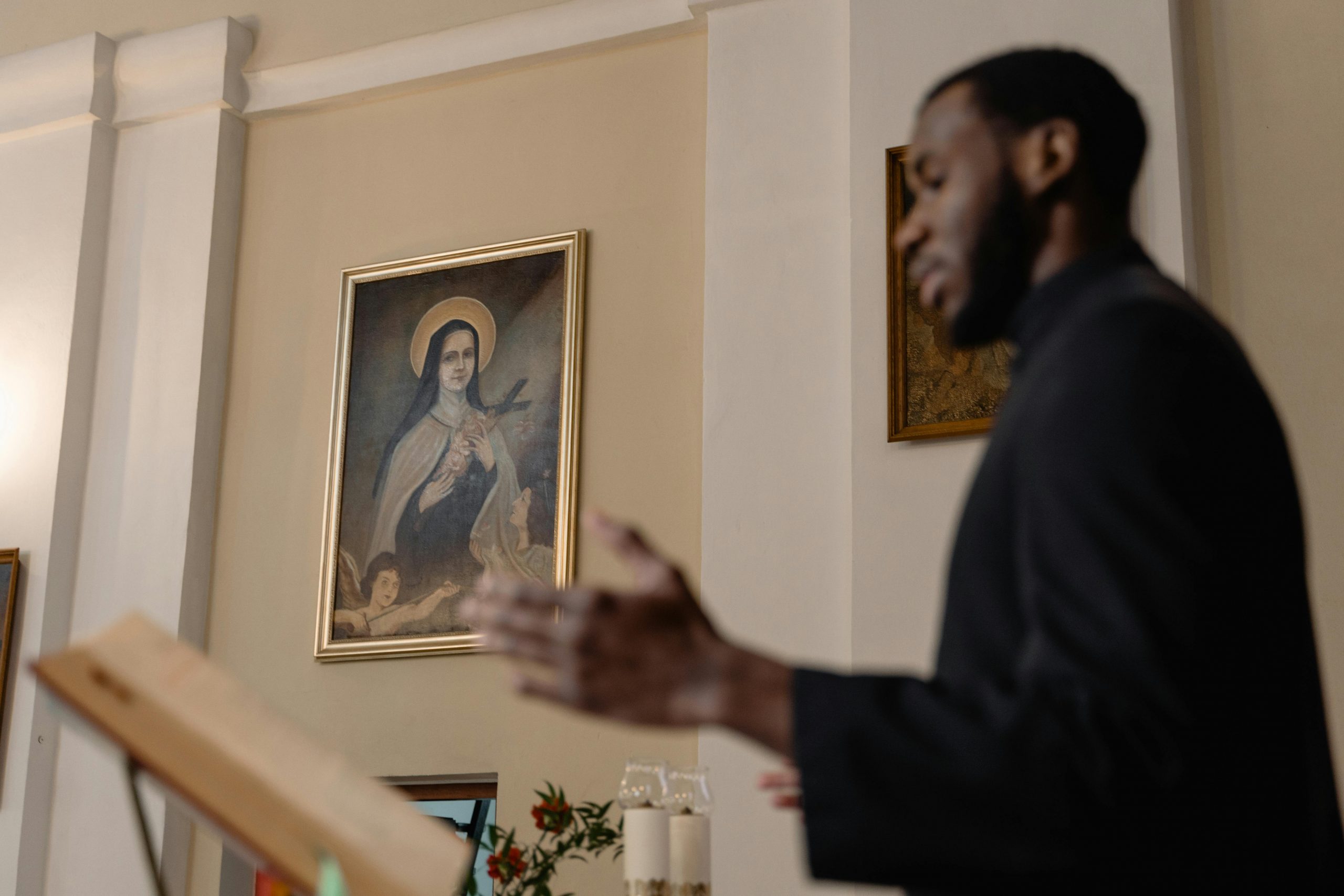 A priest delivers a sermon inside a church with religious art in the background.