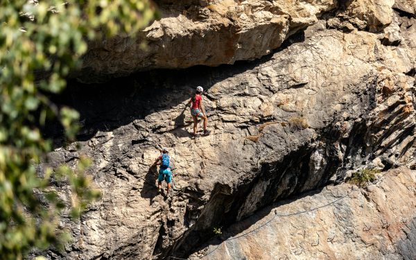Two climbers scaling a rugged mountainside on a challenging via ferrata route. Adventure and skill showcased.