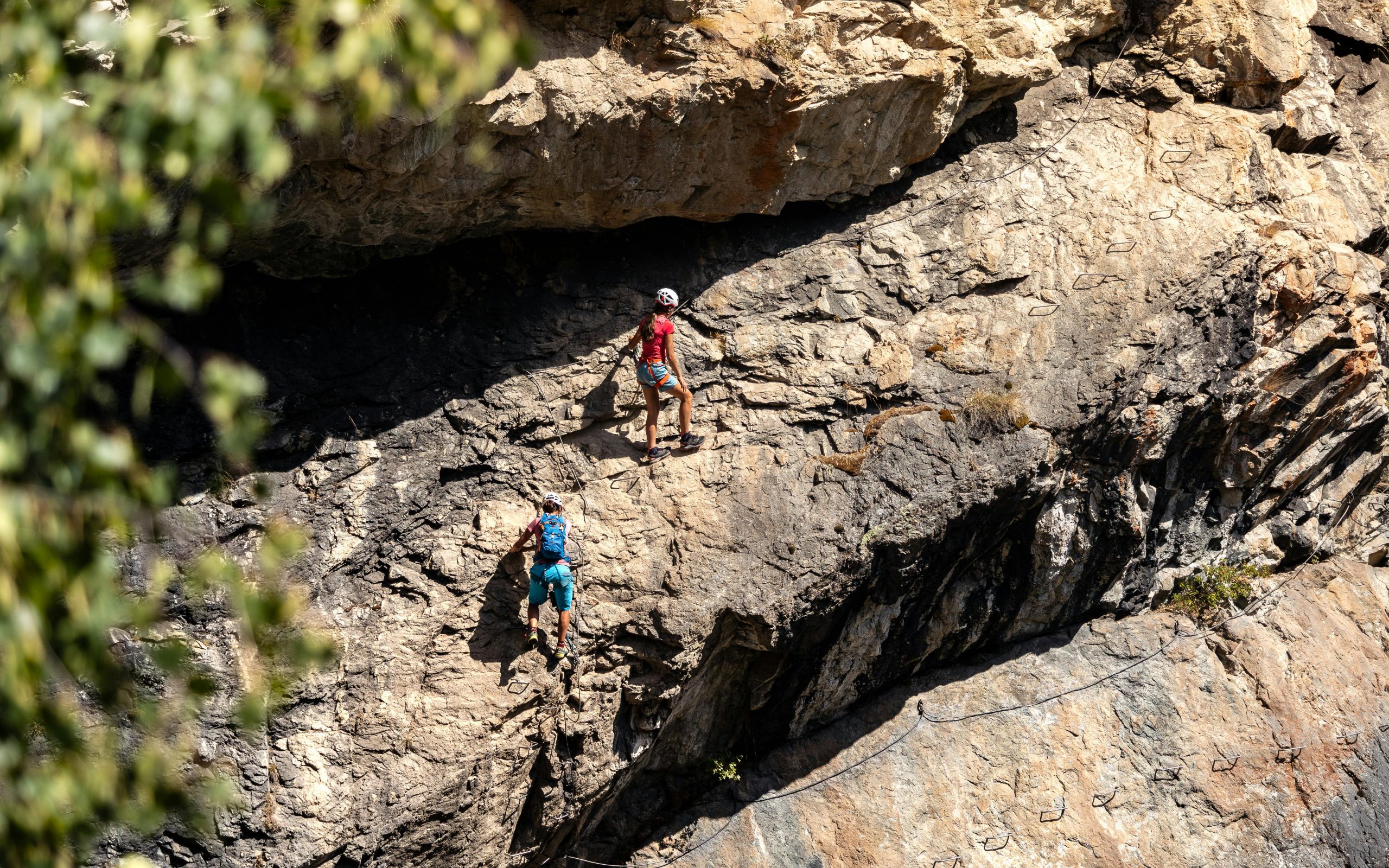 Two climbers scaling a rugged mountainside on a challenging via ferrata route. Adventure and skill showcased.