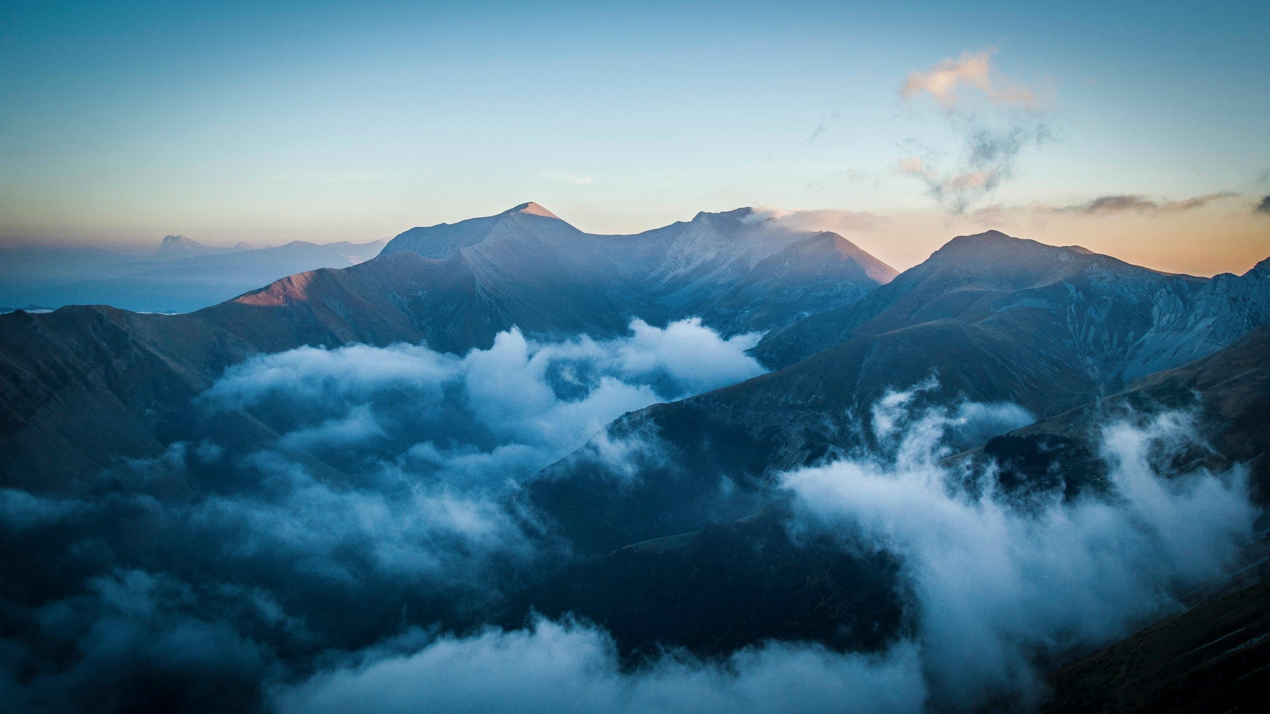 Serene mountain landscape with clouds enveloping peaks at dawn, captured in Montemonaco, Italy.