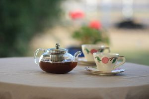 Artistic still life of floral porcelain teacups and glass teapot on a table outdoors.