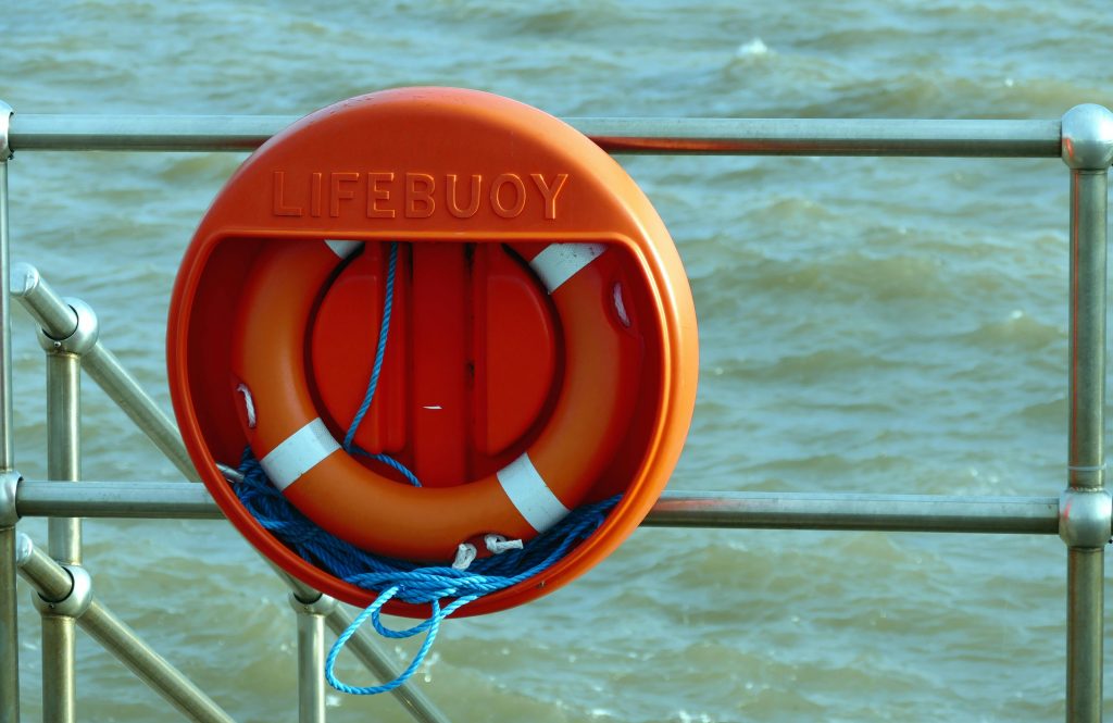 A bright orange lifebuoy hangs on a metal railing overlooking the sea, signifying safety at the coast.