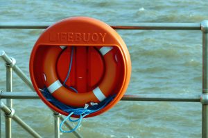 A bright orange lifebuoy hangs on a metal railing overlooking the sea, signifying safety at the coast.