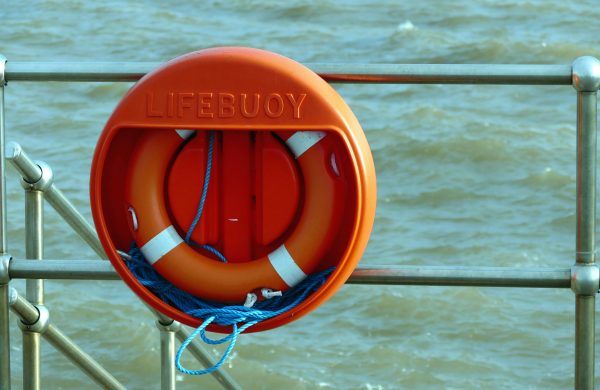 A bright orange lifebuoy hangs on a metal railing overlooking the sea, signifying safety at the coast.