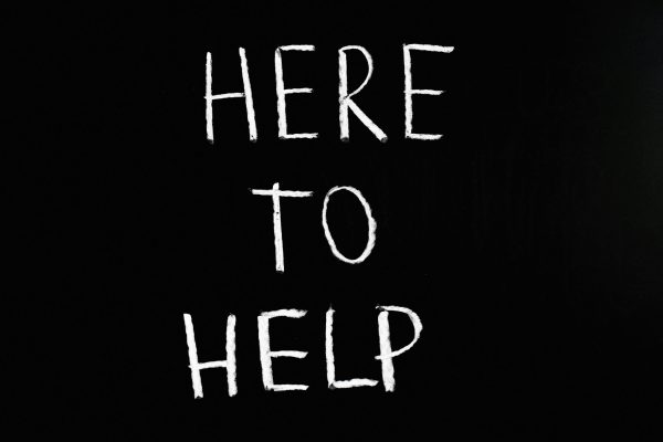 White text 'Here to Help' on a minimalist black chalkboard background, conveying encouragement and support.