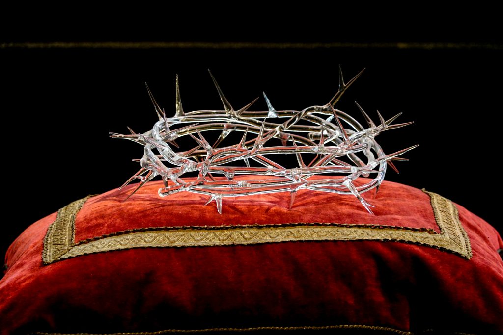 Intricate glass crown of thorns resting on a luxurious red velvet cushion.