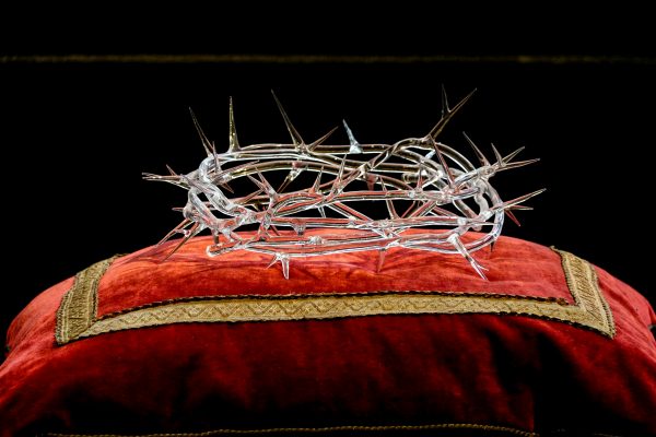 Intricate glass crown of thorns resting on a luxurious red velvet cushion.