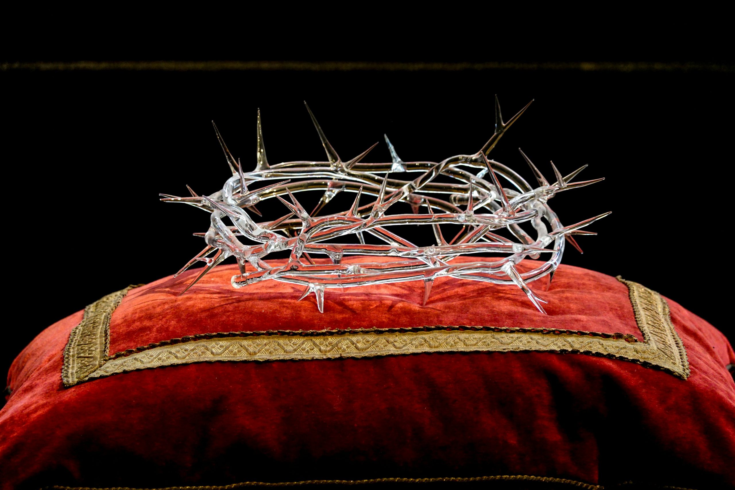 Intricate glass crown of thorns resting on a luxurious red velvet cushion.