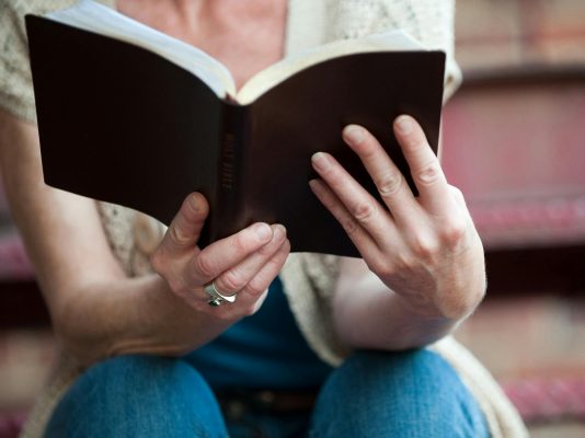 Hands holding an open Holy Bible, symbolizing faith and spirituality.