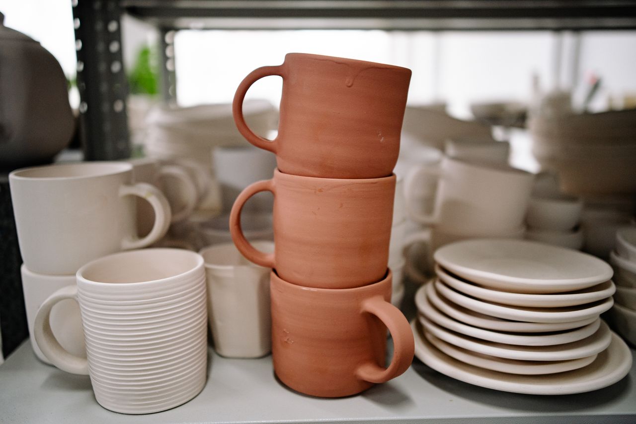 Close-up of stacked handmade ceramic mugs and plates showcasing pottery craft in a studio setting.